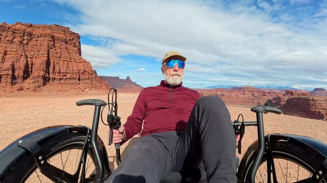 Senior cyclist is riding a full suspension recumbent tricycle off road at Thelma and Louise Point overlooking Colorado River canyon near Moab, Utah