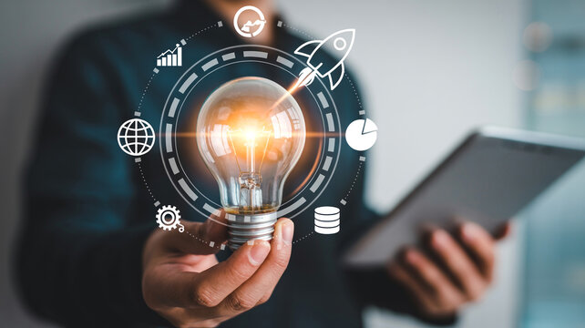Man holding a glowing light bulb with a tablet in hand, encircled by icons representing business and technology concepts
