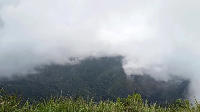 A wide, cinematic view of clouds and thick fog rolling over a deep green valley and mountain ridges. Dramatic and atmospheric nature landscape.