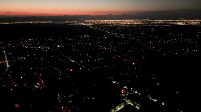 Aerial Drone View of City Lights Glowing at Dusk with mountains in the background