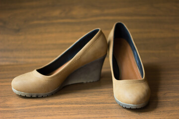 Naklejka premium Pair of tan suede women's wedge heel shoes on a brown wooden background