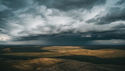Fototapeta premium Displaying dramatic storm cloud bank moving over sunlit plains, showing rain shaft and dirt tracks