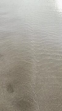 Abstract ripple patterns on wet beach sand with gentle tide movement. Minimal, calming scene ideal for backgrounds and nature visuals.