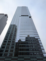 Naklejka premium Reflective glass skyscraper towering above older New York buildings, capturing the blend of modern and traditional architecture in the city, travel USA