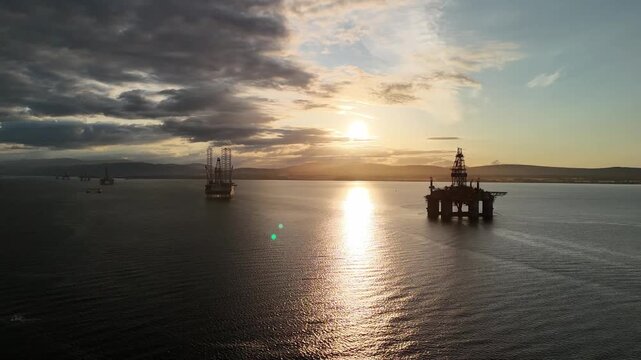 Drone pull back over oil rig graveyard at sunset in Cromarty Firth