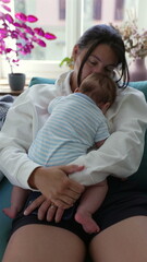 Obraz premium Mother embracing baby on sofa, kissing baby’s head, baby resting on chest, moment of deep connection and warmth in peaceful home setting