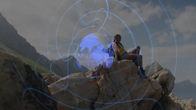 Woman sitting on cliff above coast, camera widening sparking globe showing travel sweeping over her