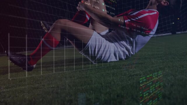 Male soccer player clutching knees on turf after injury, sports data overlays scrolling over player
