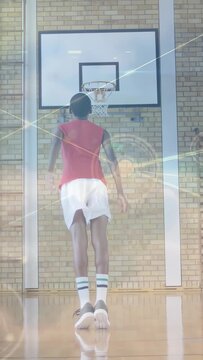 Vertical video: Teenager practicing basketball in gym, raising, jumping, releasing to hoop, overlay