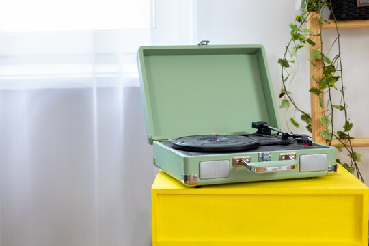 Vintage green record player with vinyl record on yellow table in a modern cozy interior with houseplants. Stylish retro music concept, home decor, analog sound and nostalgia lifestyle with copy space.