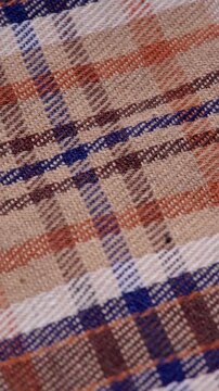 Vertical video of brown and blue plaid fabric sliding gently across the frame, Close-up of a moving tartan pattern cloth with warm earth tones in portrait orientation