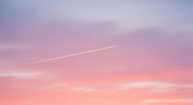 A single airplane contrail streaks across a pastel pink and purple sunset sky gradient background.