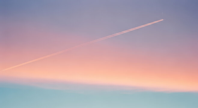 A thin airplane contrail streaks diagonally across a vast sky gradient transitioning from soft pink and peach tones to pale blue.