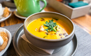 Pumpkin soup served on table. Pumpkin cream soup with seeds and greens. Cozy atmosphere.