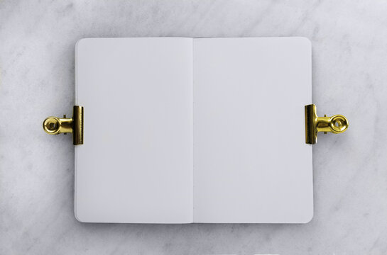 Open blank notebook with gold binder clips on marble