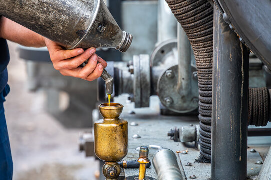Close-up of hands pouring oil into a vintage brass lubricator on a steam engine during maintenance.