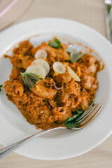 Fototapeta premium Delicious curry dish served on a white plate with shrimp, herbs, and onions in a dining setting