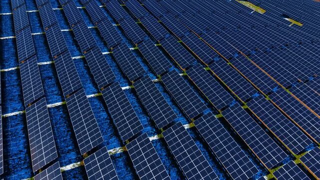 Close up aerial view of solar panel rows in winter. High angle view of photovoltaic modules with patches of white snow on the ground between rows.
