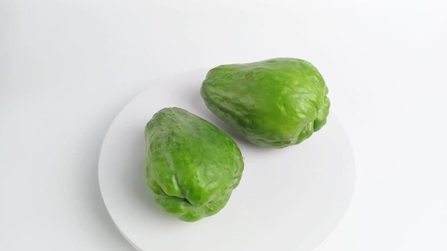 Two fresh green chayote or Sechium edule rotating on white podium, healthy vegetable food ingredient concept.
