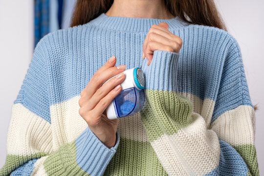 Woman using modern fabric shaver on knitted sweater sleeve removing lint and pilling. Concept of clothing renewal and garment refresh routine, extending clothing life and maintaining wardrobe quality