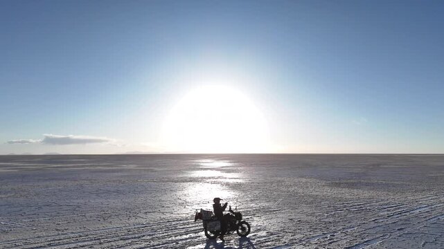 Man riding adventure motorcycle on Salar de Uyuni. Endless white landscape and rider on the vast Bolivian salt flats.