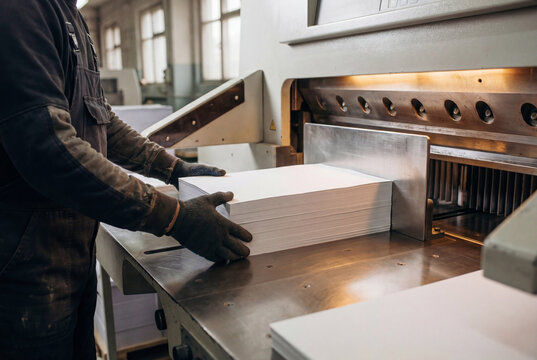 Worker hands placing white paper stack into industrial cutting machine