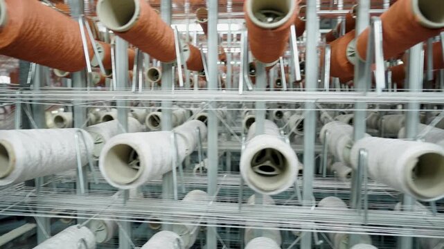 Rows of white and orange yarn spools on metal racks in an automated textile factory workshop