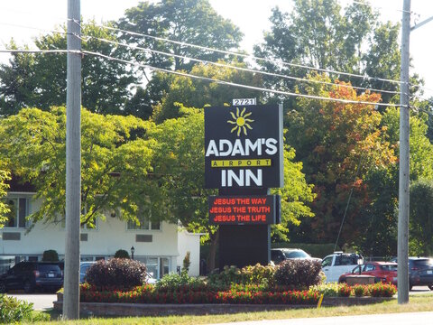 Ottawa, Ontario, Canada-July 19, 2025: A black pylon sign for "Adam's Airport Inn" at 2721 Bank Street features a sun logo and religious messaging.