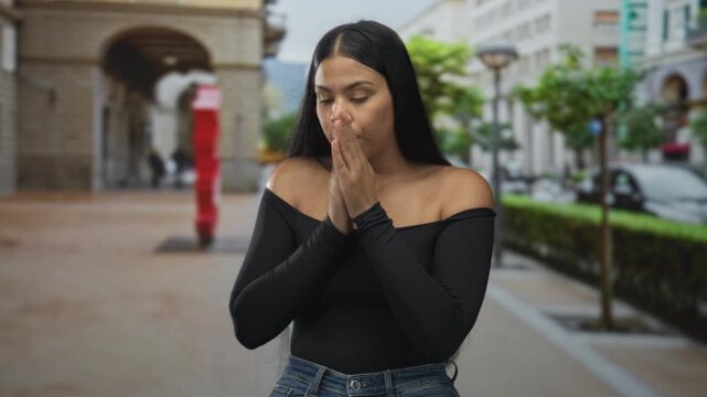Latin woman hugging arms on street pavement lined with arches and lampposts in daylight; vulnerability.
