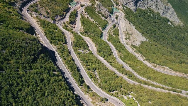 Aerial forward flight with gimbal tilt down over winding SH20 mountain road, top down view of switchbacks in Albania
