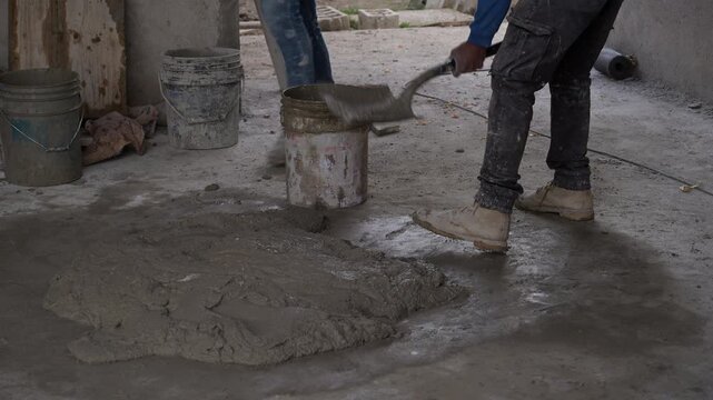 Close-up of a construction worker pouring wet cement with a shovel inside a bucket