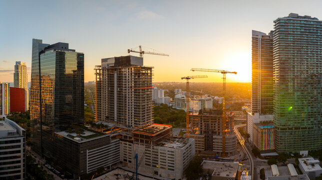 Real estate development in Miami urban area. Tower lifting cranes at high residential apartment building construction site at sunset