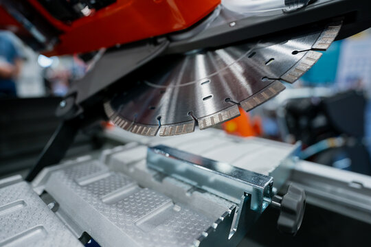Close up of a segmented circular saw blade on industrial cutting equipment, with metal work table and guide rail visible at an indoor expo hall