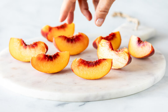 Sliced segments of free stone peaches on a marble slab with a hand reaching in.