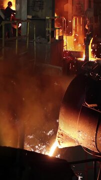 Liquid metal in the foundry, melting iron in furnace, steel mill. Worker with goggles and helmet watching and controlling iron smelting in furnaces