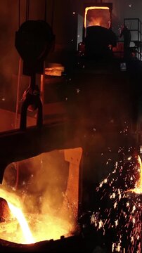 Liquid metal in the foundry, melting iron in furnace, steel mill. Worker with goggles and helmet watching and controlling iron smelting in furnaces