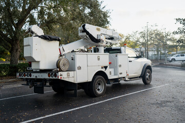 White aerial lift service truck parked in a Florida parking area with folded bucket boom, utility compartments, tree canopy, and leaf scattered pavement © K