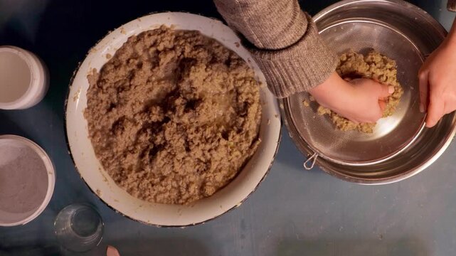 Step 3 of papier mache process. Hands squeezing soaked recycled paper pulp to remove water and prepare material for handmade craft mixture