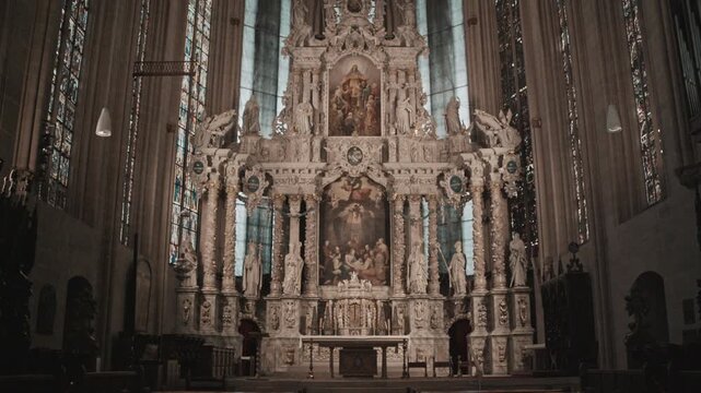 Interior of historic cathedral in Erfurt, Germany, featuring an ornate baroque altar, statues, and tall stained glass windows. Majestic Christian church architecture with rows of wooden pews