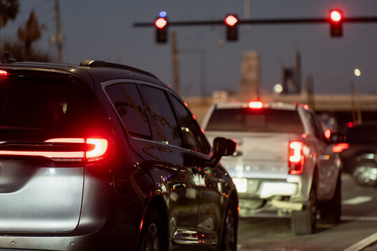 Rear view of USA evening traffic stopped at a red light, with a dark SUV, white pickup, brake lights, and a busy multi lane roadway ahead at dusk