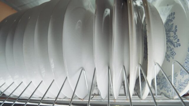 Clean White Plates Stored on Metal Dish Rack Inside Kitchen Cabinet | Ceramic Dinnerware with Blue Floral Pattern | Close-Up Domestic Kitchen Storage