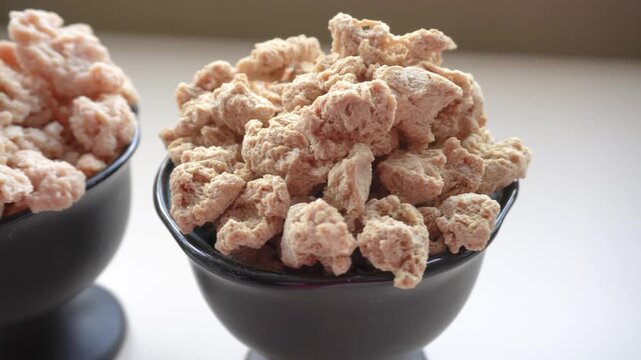 two black bowls with soaked soy meat and dry. On the left is a bowl with pieces of dry soy with a looser and more porous consistency. Soaked soy meat on the right.