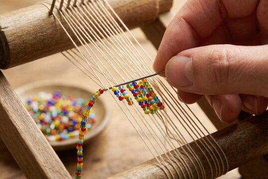 Close up of fingers weaving a pattern of colorful glass seed beads on a small wooden loom
