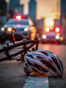 Bike accident scene with damaged helmet and fallen bicycle on street as emergency vehicles arrive at sunset in urban environment