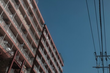 Obraz premium Red apartment building with balconies and power lines against blue sky in Japanese city