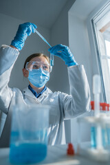 Young researcher in lab coat and safety goggles works with test tubes, focusing on precise...