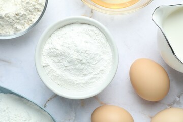 Baking powder and other ingredients for making dough on white marble table, flat lay