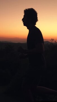 Silhouette of man running on grassy hill at golden hour sunset sunrise