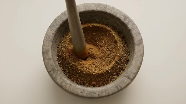 A stone mortar with a wooden pestle grinds dried herbs and spices