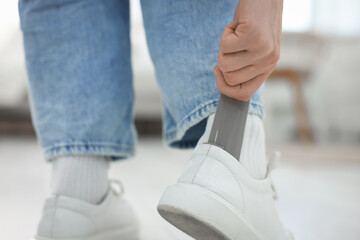 Obraz premium Woman putting on stylish sneakers with shoehorn at home, closeup